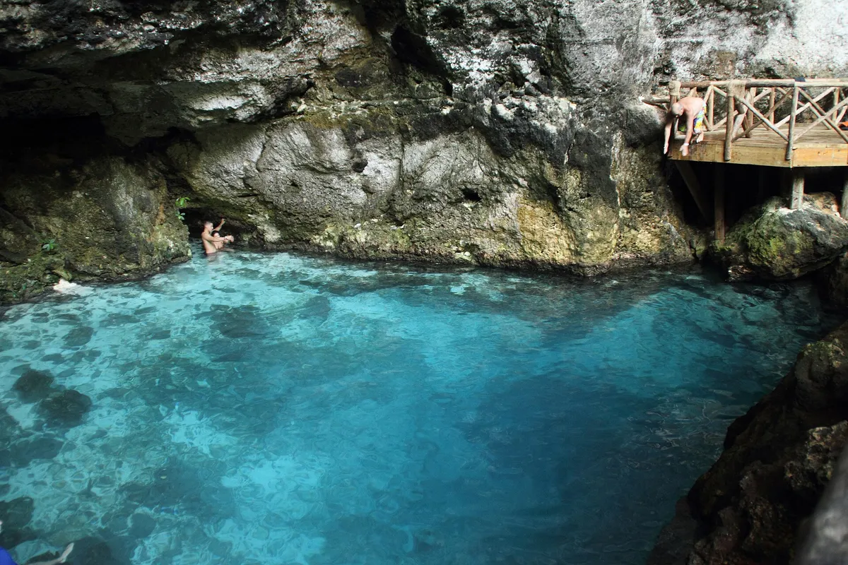 The turquoise water of Hoyo Azul cenote surrounded by limestone rock and jungle in Cap Cana